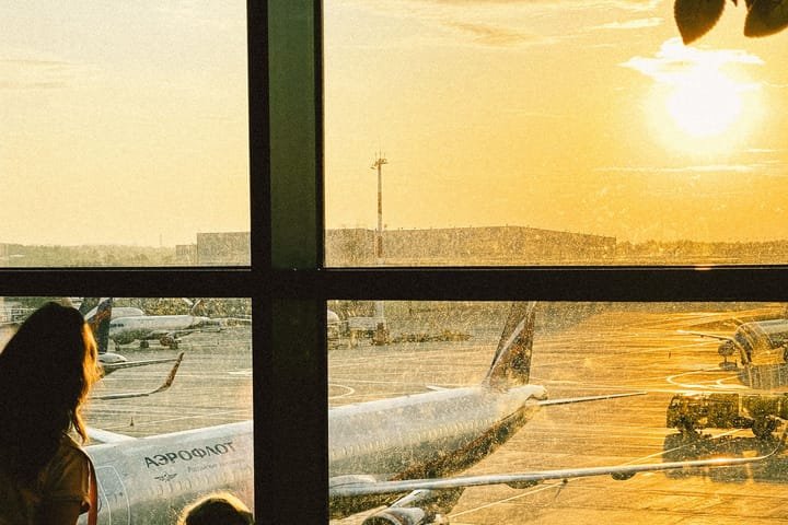 A mother and her daughter watching the planes through an airport window at sunrise
