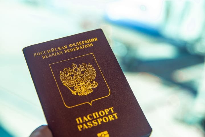 A hand holding a passport at an airport gate, an aircraft blurred behind the window